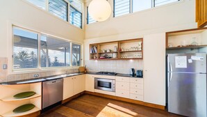 Cocina moderna con lavavajillas, horno y refrigerador. Cuenta con un ventanal grande y estantes de madera sobre la encimera.