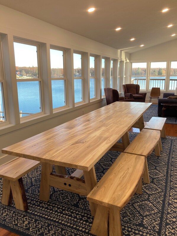 Une longue table en bois, des bancs, de grandes fenêtres donnant sur un lac et un tapis à motifs.