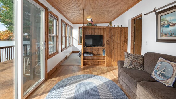 Een ruime woonkamer met houten plafond, grote ramen, een televisie en een gezellige bank.