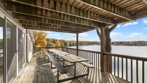 A wooden deck with picnic tables overlooking a lake. - Huge lake house. 3 levels. 10 bedrooms. Great for groups. Large beach. Fire pit. (Newaygo)