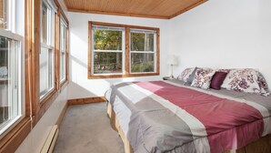 Een slaapkamer met een groot bed, houten plafond en een raam met uitzicht op bomen.