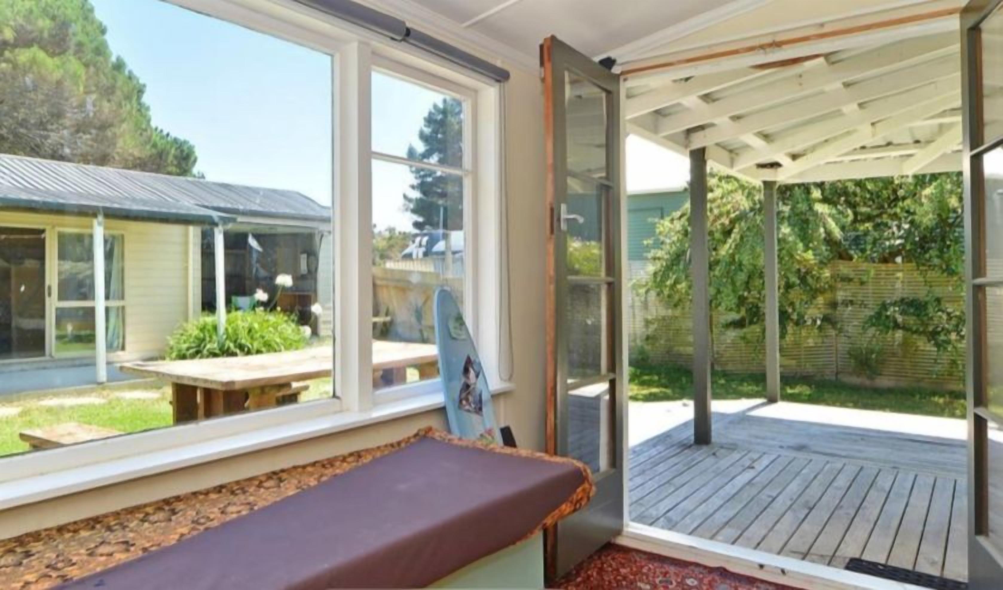 A room with a bed, a window, and a view of a house and garden.