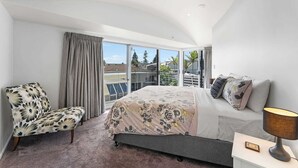 Une chambre à coucher avec un lit, une chaise, une table de chevet et de grandes fenêtres.