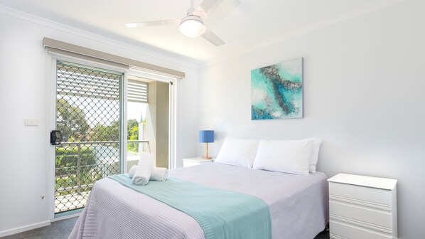 A bedroom with a bed, a nightstand, a lamp, a ceiling fan, and a sliding glass door leading to an outdoor area. - Blue Pacific 2 offering stunning ocean views (Yamba)