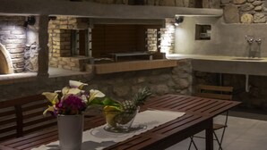 Eine Küche mit Steinwänden, einem eingebauten Ofen und Spüle, Holzbänken und einem Tisch mit Blumen in einer Vase.