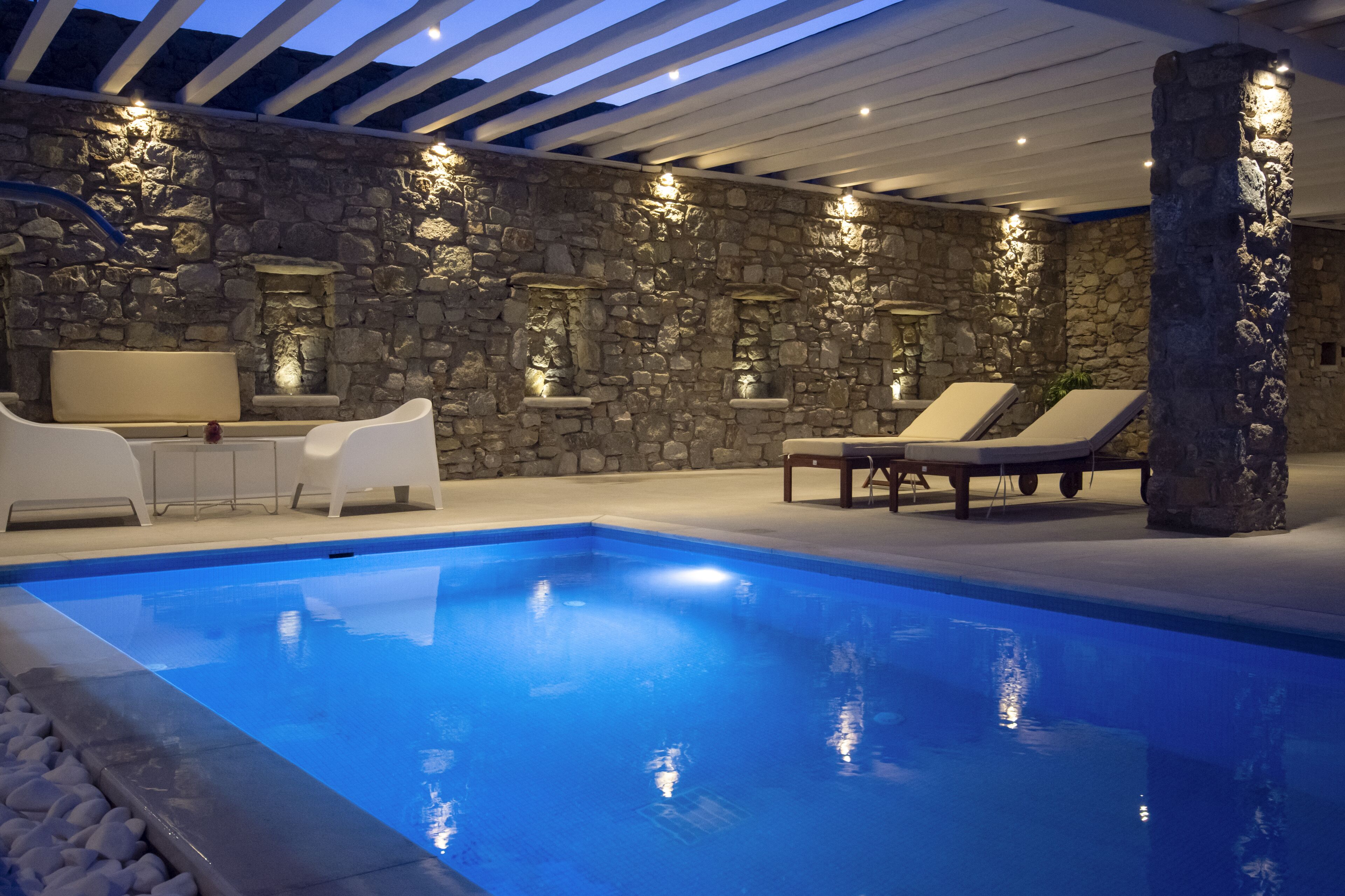 A pool area with stone walls, white lounge chairs, and a ceiling with wooden beams.