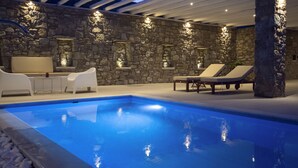 Ein Poolbereich mit Steinmauern, weißen Liegestühlen und einer Decke mit Holzbalken.