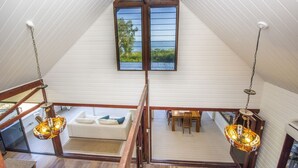 Ein Loft-Zimmer mit hohen Decken, Holzbalken, einem weißen Sofa, einem Esstisch und einem großen Fenster mit Blick.