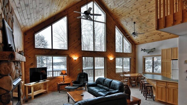 A spacious living area with a stone fireplace, large windows, a black leather couch, and a dining area.