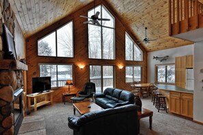 A spacious living area with a stone fireplace, large windows, a black leather couch, and a dining area.