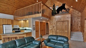 A spacious living area with a wooden ceiling, a kitchen with modern appliances, and a staircase leading to an upper level.