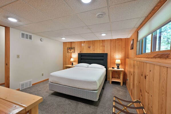 A bedroom with a large bed, wooden walls, a window, and a desk.