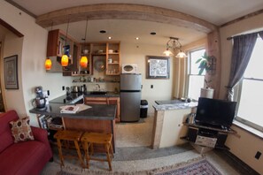 Una cocina compacta con una isla central, un área de comedor con un sofá rojo y un televisor sobre un soporte.
