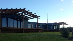 A modern building with a wooden pergola, large windows, and a grassy area. - Private stunning elevated ocean veiws (Whangapoua)