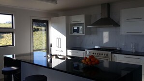 A modern kitchen with a central island, a stove, an oven, and a microwave. There are two windows providing natural light and a view of the outdoors. - Private stunning elevated ocean veiws (Whangapoua)