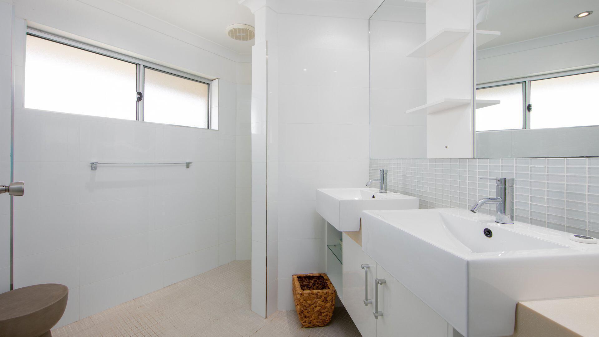 A modern bathroom with two sinks, a large mirror, and a window.