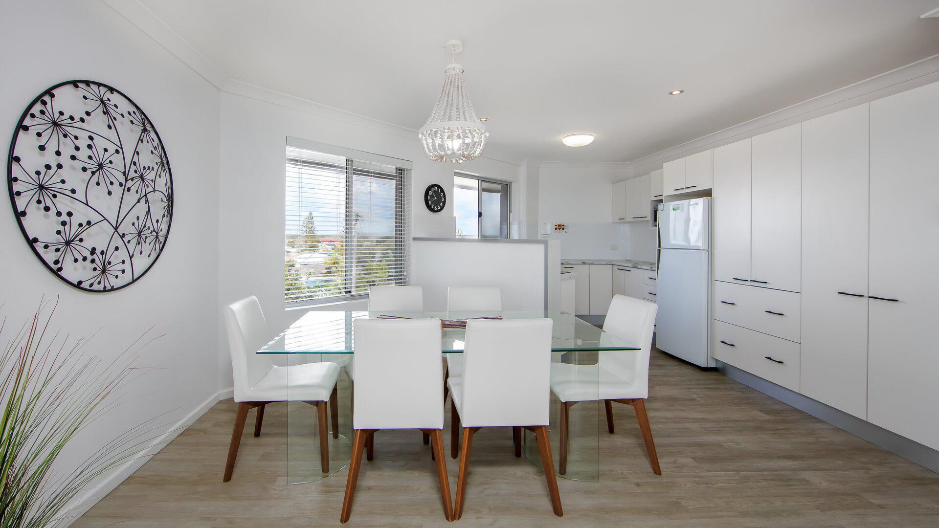 A modern kitchen with white cabinetry, a glass dining table, and a chandelier.