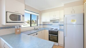 A modern kitchen with white cabinets, a microwave, a stove, and a refrigerator. - Flinders Lodge - an idyllic holiday rental (Yamba)
