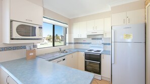 Enjoy a kitchen with a microwave, refrigerator, stove, and sink, offering a view of palm trees outside.