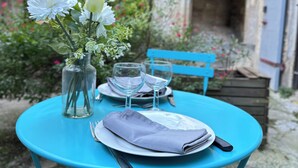 Ein Tisch draußen gedeckt mit einem Blumenstrauß, zwei Weingläsern, einem gefalteten Servietten und Besteck.