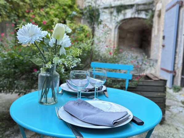 A table set outdoors with a vase of flowers, two wine glasses, a folded napkin, and cutlery.