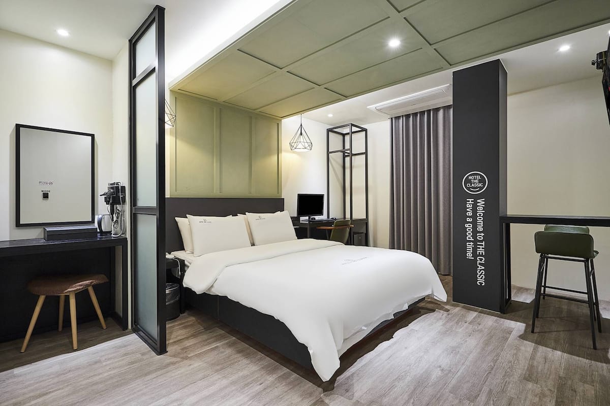 Quarto de hotel moderno com uma cama grande, uma escrivaninha, uma cadeira e um espelho.