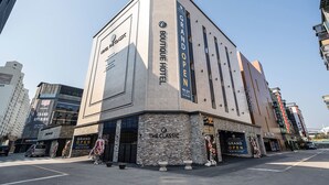 Un hôtel appelé « The Classic », doté d’un design moderne, avec une enseigne bien visible annonçant son « inauguration officielle » et une façade ornée de grandes fenêtres.