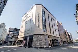 Un hotel llamado "The Classic", con diseño moderno, que muestra un letrero destacado que anuncia "Gran Inauguración" y una fachada con grandes ventanales.