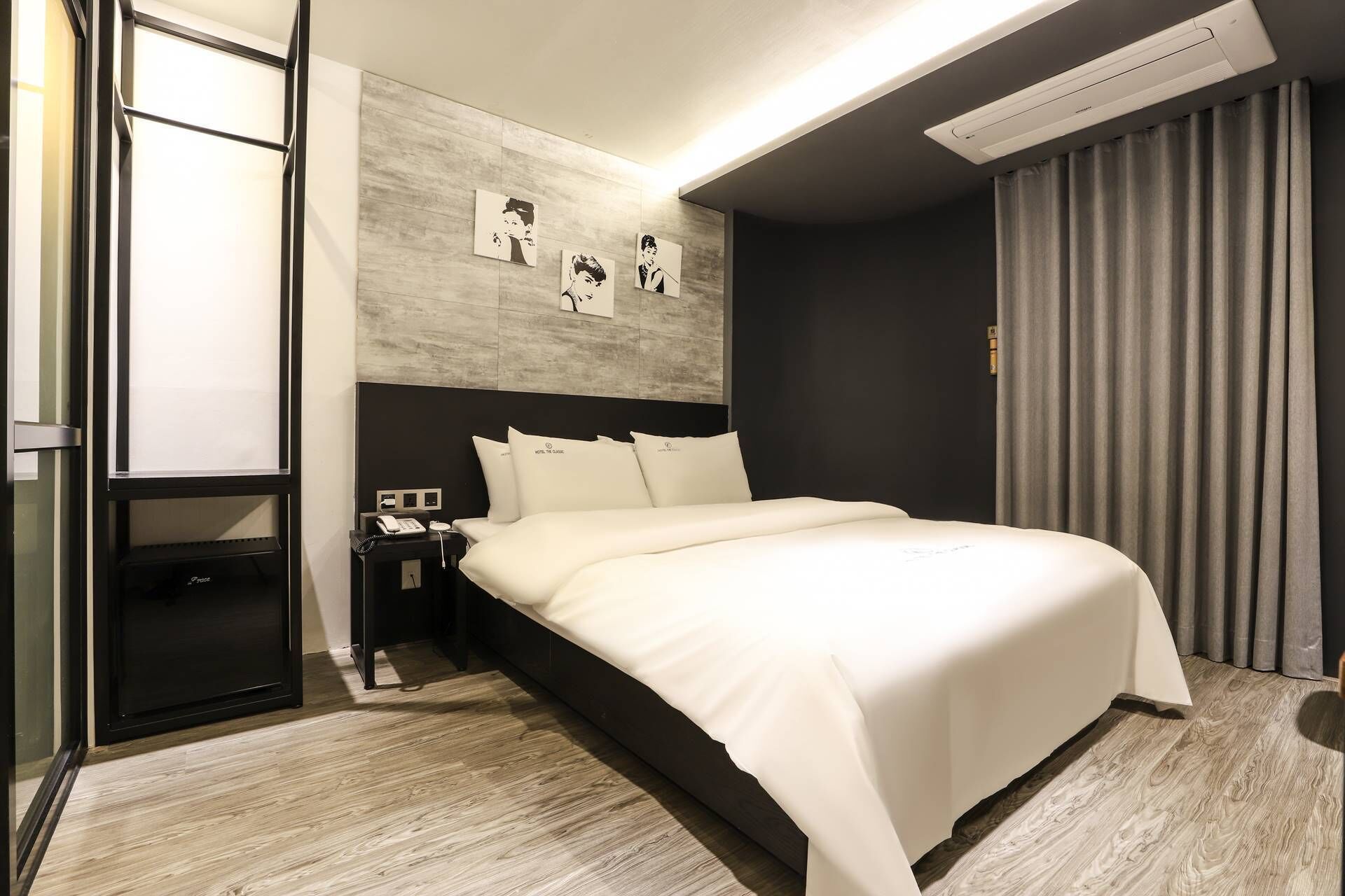 Et moderne hotelværelse med en stor seng, et natbord med telefon og en vægmonteret klimaanlæg.