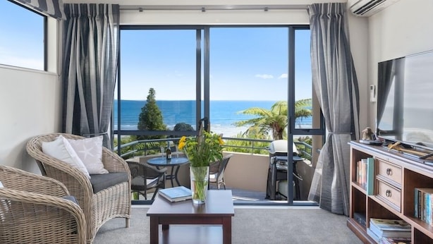 Un balcon avec vue sur l’océan, des meubles en osier, une table avec un vase et une bibliothèque.