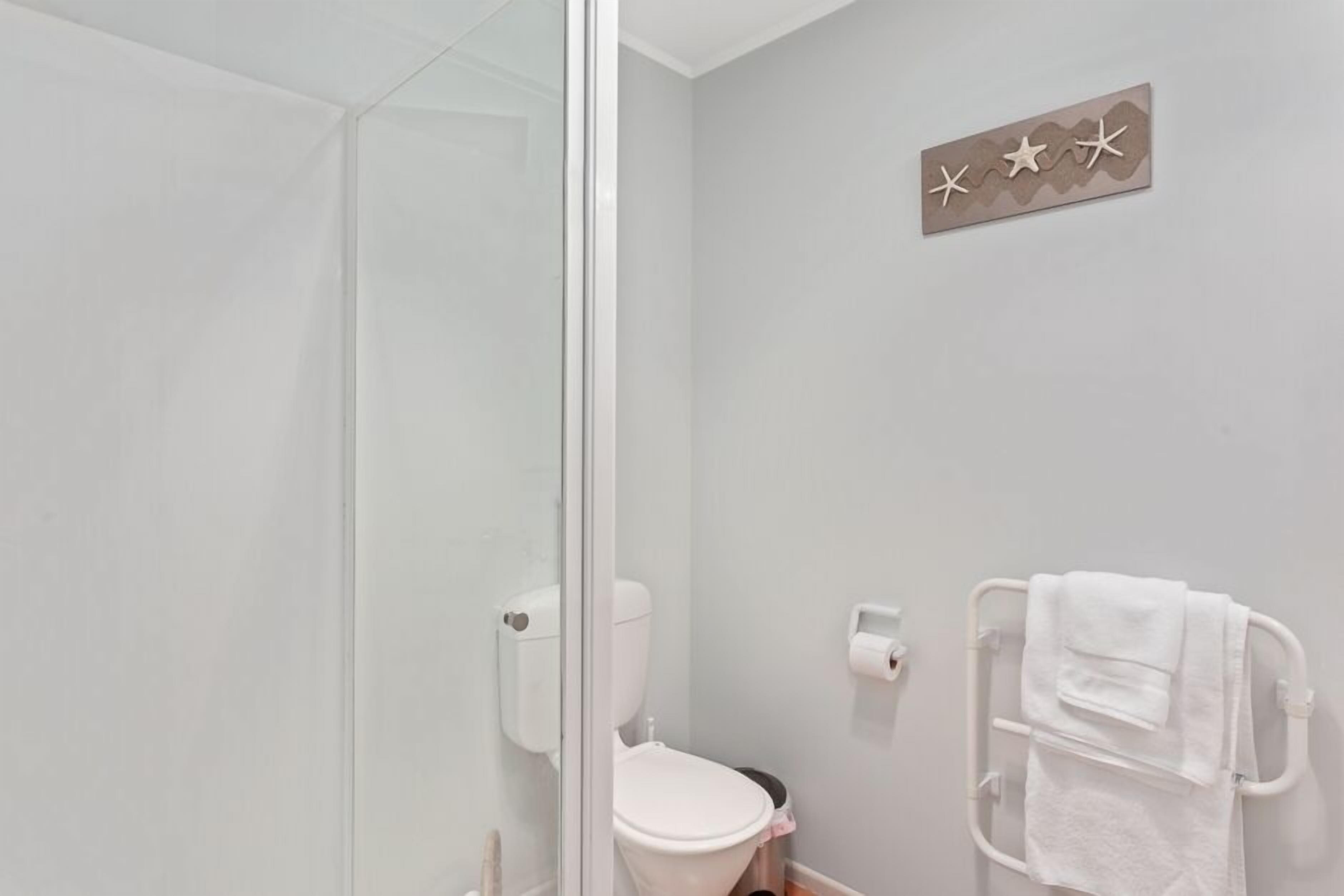 Un baño con cabina de ducha de vidrio, inodoro y toallero con toallas.
