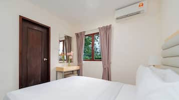 A hotel room with a bed, a desk, a mirror, a window with curtains, and an air conditioning unit.