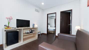 A hotel room with a television, a small refrigerator, a sofa, and a bedside table.