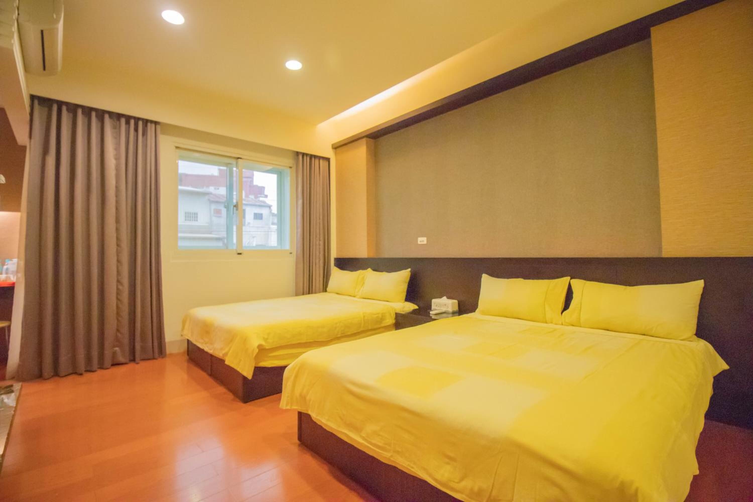 A hotel room with two beds, a large window, and a view of buildings outside.