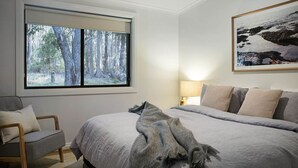 Une chambre avec un grand lit, une chaise, une fenêtre donnant sur une forêt et un tableau accroché au mur.