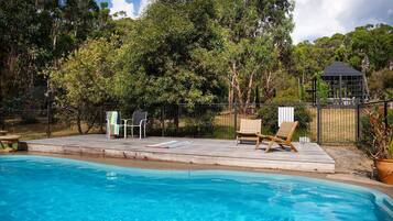 A poolside area with a wooden deck, two lounge chairs, and a small table.