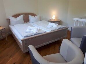 Un lit bien fait, avec des oreillers et une serviette pliée, une table de chevet avec une lampe et une chaise dans une pièce au plancher en bois.