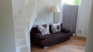 Una sala de estar moderna con un sofá marrón, cojines estampados, una lámpara de pie y una escalera.