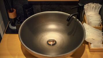 A modern bathroom with a large, round sink, a mirror above it, and a wooden tray holding toiletries.