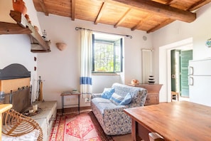 A cozy room with a wooden ceiling, a window with curtains, a patterned sofa, a wooden table, and a radiator.