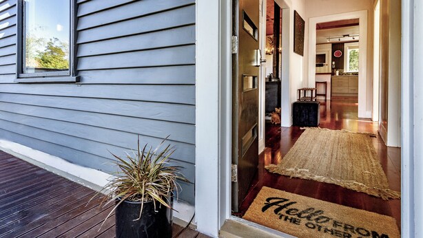 A house entrance with a wooden deck, a potted plant, and a welcome mat.