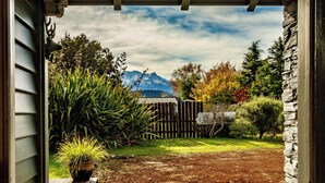 A wooden deck leading to a garden with a mountain view, a wooden fence, and a stone wall.