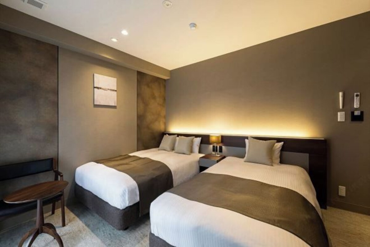 A hotel room with two beds, a bench, and a small table.