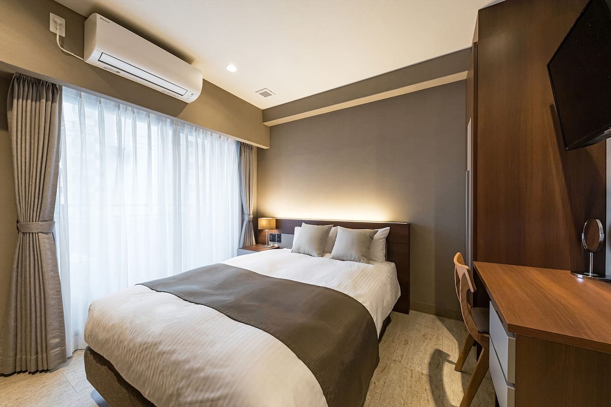 Una habitación de hotel con una cama grande, un escritorio, un televisor y un aire acondicionado.