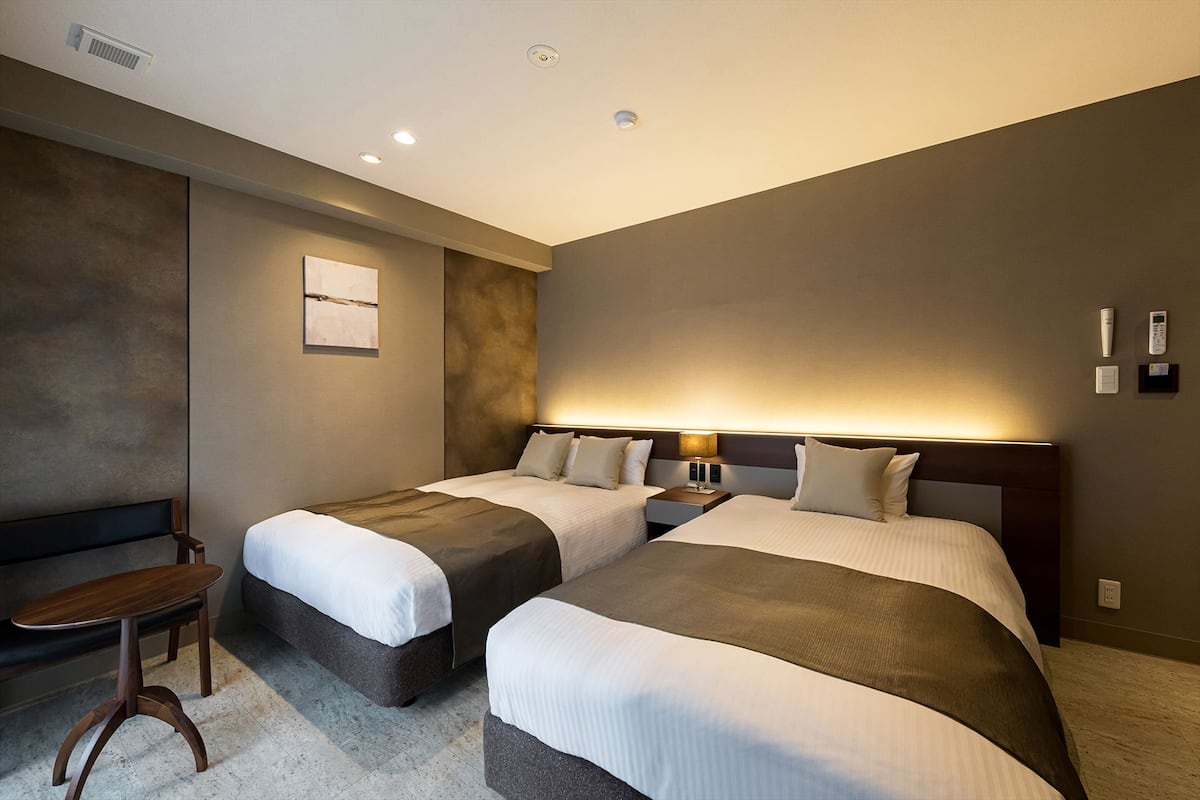 Una habitación de hotel con dos camas, una mesita y un banco.