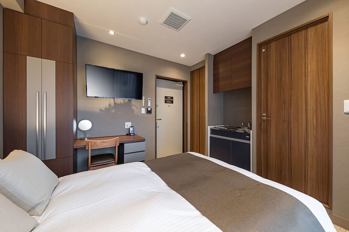 Una habitación de hotel con una cama, un escritorio con computadora, un televisor y un armario.