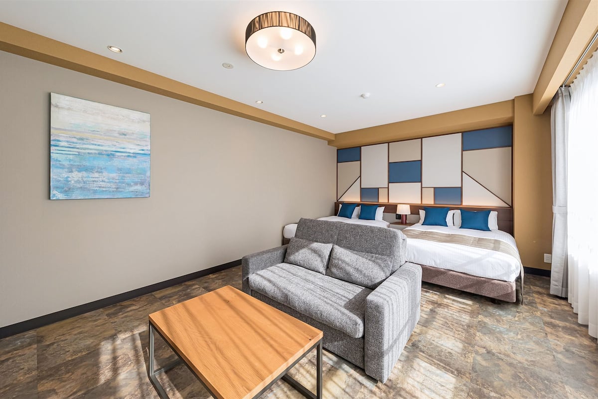 Habitación de hotel con sofá, una mesa de madera, cama con cabecera geométrica y un cuadro en la pared.