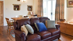 A cozy living room with a brown leather sofa, a wooden dining table, and a stone fireplace. - High Dalton Hall Cottage (Newsham, near Richmond)