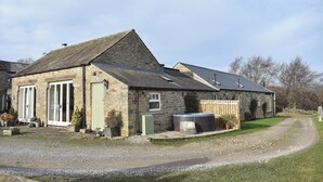A stone building with a sloped roof, a large window, and a small garden area with gravel and potted plants. - High Dalton Hall Cottage (Newsham, near Richmond)