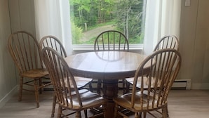 Une table à manger entourée de six chaises en bois, une fenêtre avec des rideaux et une vue sur une forêt.